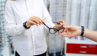 Optisyen, optometrist, göz doktoru ya da göz doktoru elinde gözlük ve gözlüklerle yeni gözlük tutuyor. Klinikte ya da dükkanda elinde gözlüklerle profesyonel görme uzmanı. Çift odaklı ya da çok odaklı gözlük.