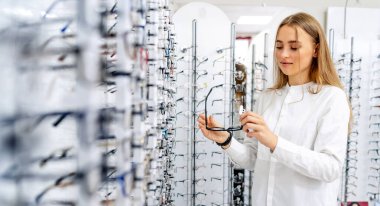 Young woman is choosing glasses in optician store. Eyesight correction. Ophtalmologist concept.