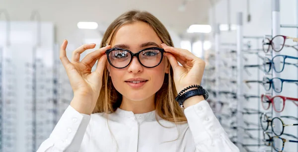 Happy female client or optician is standing with set of glasses in background in optical shop. Woman in spectacles. Girl wearing glasses. Portrait of a woman in correcting glasses. Closeup. — Stockfoto