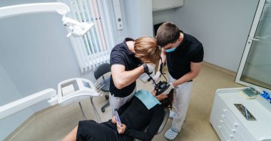 Diş aletleri olan iki erkek dişçi, dişçi muayenehanesinde hastanın dişlerini tedavi ediyor. Tıp, dişçilik ve sağlık hizmetleri konsepti. Ağız bakımı. Yan görünüm.