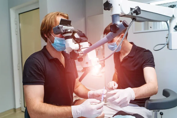 Male dentists with microscope checking up patient\'s teeth at modern dental clinic office. Medicine, dentistry and health care concept. Dental equipment
