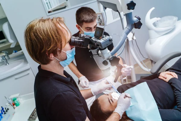 Dentistas machos com microscópio verificando os dentes do paciente no consultório odontológico moderno. Medicina, odontologia e conceito de cuidados de saúde. Vista do lado. — Fotografia de Stock