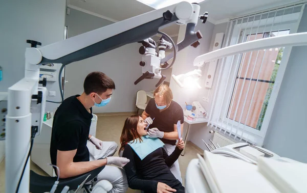 Dentistas do sexo masculino examinando a mulher jovem olhando para os dentes com microscópio profissional no consultório odontológico cirurgia moderna. Focagem lateral seletiva. — Fotografia de Stock