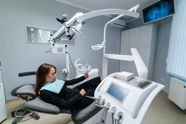 Pacjentka siedzi na krześle dentystycznym i patrzy w lustro. Nowoczesny gabinet dentystyczny. Koncepcja stomatologii. Koncepcja medycyny, stomatologii i opieki zdrowotnej. Opieka jamy ustnej. — Zdjęcie stockowe