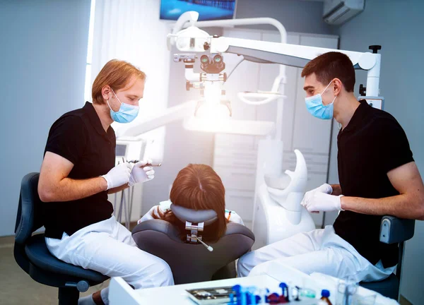 Dentistas com máscara protetora e luvas reparam dente de jovem cliente do sexo feminino em ambulante. Cuidados orais. — Fotografia de Stock