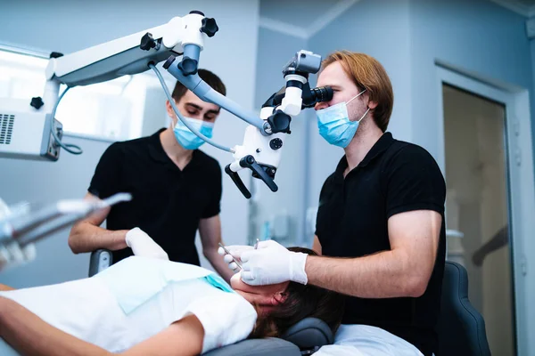 최신 앰뷸런스에 현미경으로 보호 마스크를 쓰고 장갑 수리를 한 젊은 여성 고객의 이빨을 가진 치과 의사들. 구강 관리. — 스톡 사진