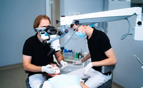 O dentista examina os dentes do paciente com um microscópio dentário. Equipamento médico moderno. Conceito de tratamento oral. Fecha a porta. Foco seletivo. — Fotografia de Stock