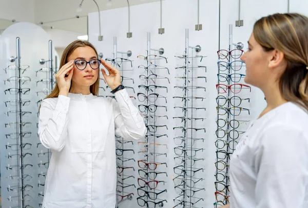 Felice cliente femminile o ottico è in piedi con set di occhiali in background in negozio ottico. Donna con occhiali. Correzione della vista. Ragazza con assistente commerciale. Occhiali correttivi. Primo piano. — Foto Stock