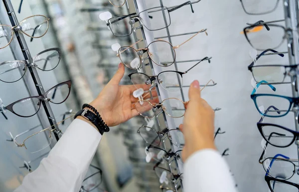 Fila de gafas en una óptica. Tienda de anteojos. Soporte con gafas en la tienda de óptica. La mujer elige los anteojos. Corrección de la vista. — Foto de Stock