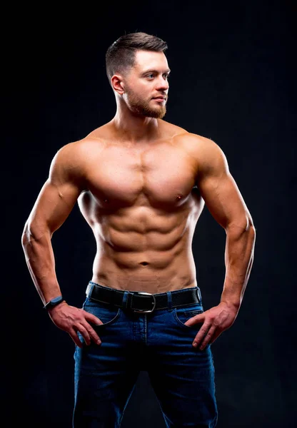 Güzel vücutlu, gömleksiz, elleri belinde poz veren. Stüdyo fotoğrafı. Kotlu yakışıklı bir adamın portresi. Yakın çekim..