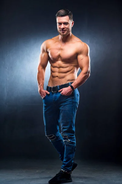 Full size photo of an athletic guy posing with hands in pokets. Studio shot. Bodybuilder. Dark grey background. Closeup. — Stock Photo, Image