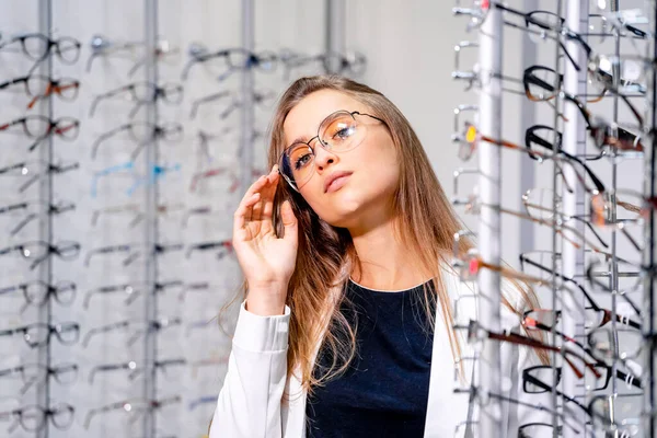 Modell flicka står med uppsättning glasögon i bakgrunden i optisk butik. Kvinnan i glasögon. Synkorrigering. Flicka klädd i glasögon. Porträtt av en kvinna i glasögon. Närbild. — Stockfoto