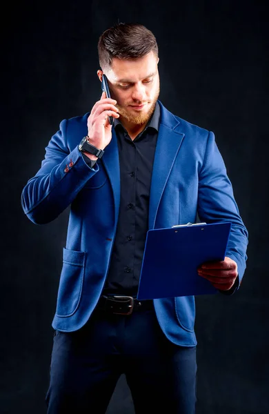 Homme d'affaires confiant parle au téléphone avec dossier à la main isolé sur fond noir en studio . — Photo