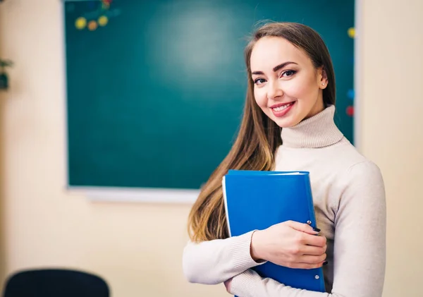 Aantrekkelijke jonge vrouw leraar in een klaslokaal onderwijs Engels taal met notities in handen. — Stockfoto