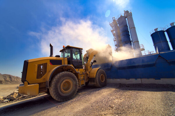 Orange wheel loader excavator in the background of a gravel storage in the open air. Quarry and mining equipment.