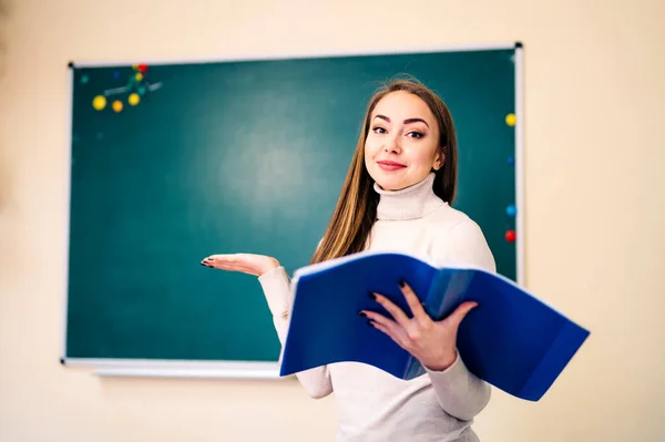 Menina estudante de pé perto de quadro-negro limpo na sala de aula com notas abertas nas mãos. Conceito de escola e educação. — Fotografia de Stock