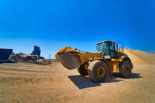 Il trattore raccoglie uno scoop con ghiaia. escavatore estrae sabbia e ghiaia per la miscela di calcestruzzo. Cielo blu sopra . — Foto Stock