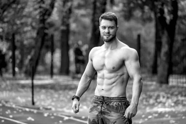 Spor sahasında poz veren atletik tişörtsüz erkek fitness modeli. Güzel kaslı vücut. Yarım yamalak fotoğraf. Kameraya bakıyorum. Yakın çekim.. — Stok fotoğraf