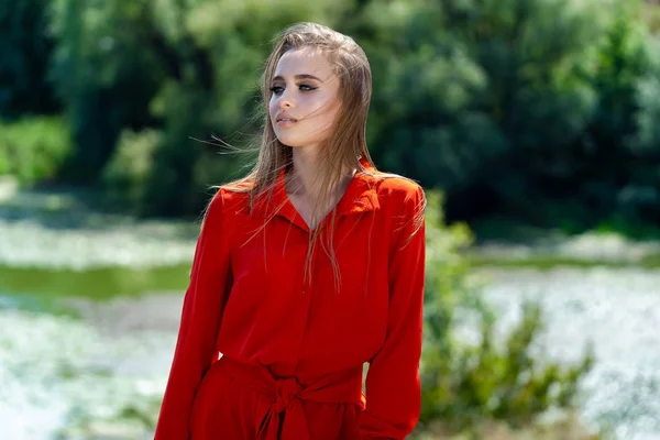 Retrato de una mujer hermosa vestida con rojas al aire libre. Joven rubia mirando hacia atrás sobre la naturaleza desdibujada. Foto mitad cansada. Cierre. — Foto de Stock