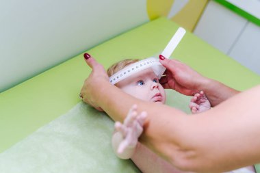 Yeni doğan bebeği muayene eden bir çocuk doktorunun fotoğrafı. Doktor, bebeğin kafa büyüklüğünü ölçmek için mezura kullanıyor. Yakın çekim..