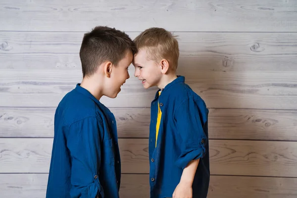 Retrato de dois irmãos de pé cabeça a cabeça em estúdio. Meninos vestindo a mesma roupa posando juntos isolado em fundo de madeira. Foco seletivo. — Fotografia de Stock