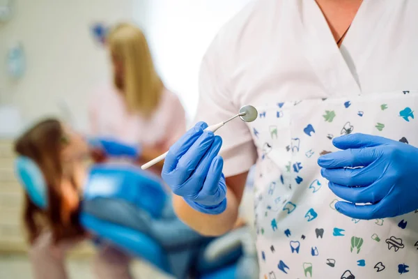 手袋の歯科医は工具鏡を持っています。歯医者の診療所にある血液検査器。チームはバックグラウンドで作業しています。選択的フォーカス。閉鎖 — ストック写真