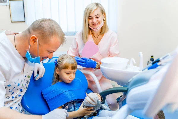 男牙医在小女孩病人面前拿着玩具。可爱的小男孩看着玩具在口腔科椅子上。儿科口腔学概念. — 图库照片
