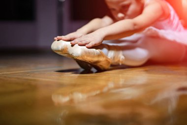 Beyaz taytlı küçük tatlı kız dans stüdyosunda yeni bir bale hareketi yapıyor. Seçici odak.