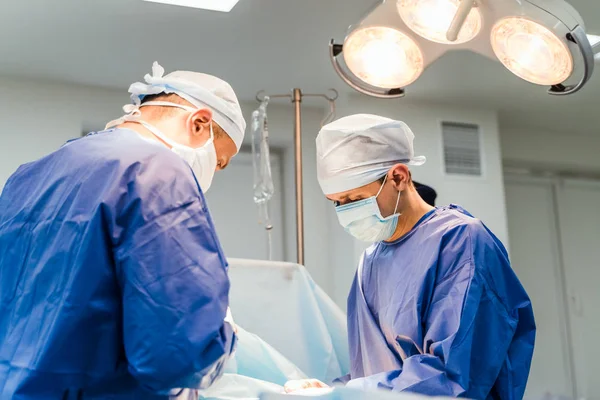 Zwei Ärzte in steriler medizinischer Kleidung führen in einem Krankenhaus eine Operation durch. Professionelle Arbeit in der Klinik. Gesundheitskonzept, Medizin. Nahaufnahme — Stockfoto