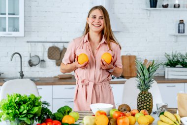 Neşeli, komik, pozitif kız göğsünün yanında iki portakal, sağlıklı meyve ve sebzelerle dolu bir masa..