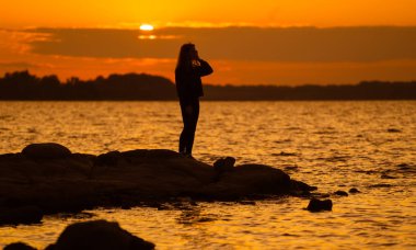 Gün batımında bir kadının silueti kayanın üzerinde dimdik duruyor. Doğa ve güzellik kavramı. Turuncu gün batımı.