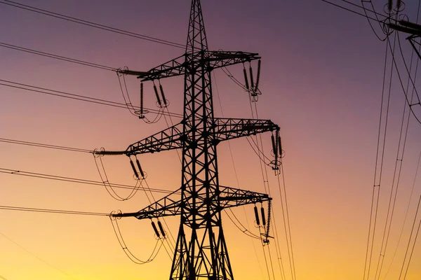 Energy Distribution Network - Electricity Pylons against Orange and Yellow Sunset. Closeup