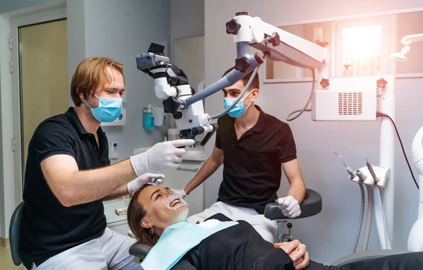 Médico dentista masculino examinando paciente olhando para os dentes com microscópio profissional no consultório odontológico cirúrgico — Fotografia de Stock