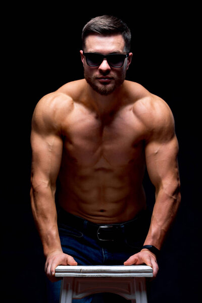 Сексуальный молодой человек на тёмном фоне позирует. Идеальное мужское тело. Руки в карманы. Мужская концепция красоты. Половина повернулась к камере. Крупный план
.