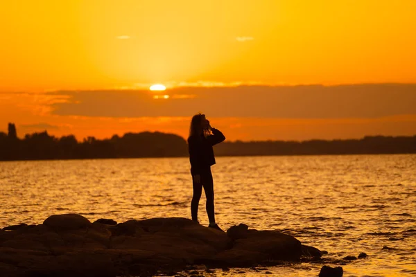 Gün batımında kadın silueti kayanın üzerinde dimdik duruyor. Doğa ve güzellik kavramı. Turuncu gün batımı.