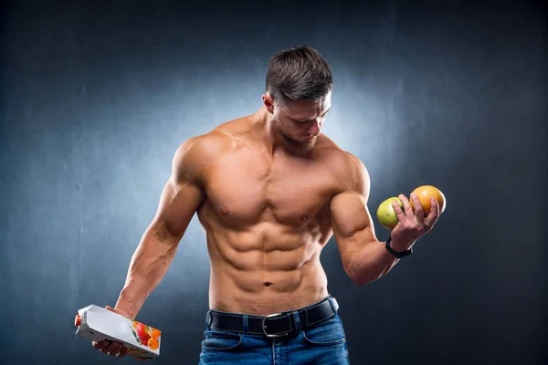 健美运动员拿着水果和果汁. 选择纯的还是浓缩的饮料。 肖像。 灰色背景。 包扎 — 图库照片