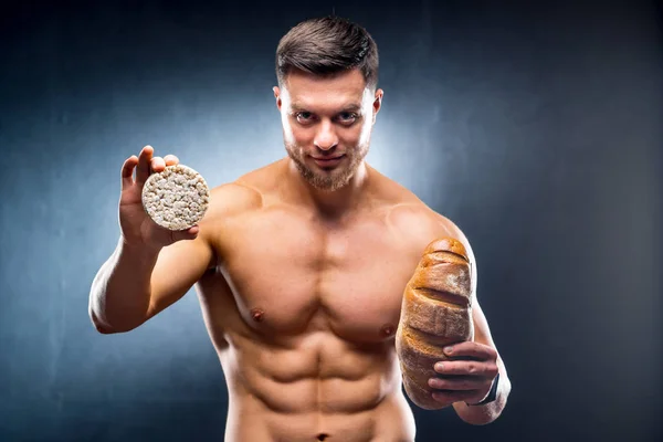 Genç çıplak adam mısır gevreği ve ekmek tutuyor. Sağlıklı ve zararlı yiyecekler arasında seçim yapmak. Yatay fotoğraf gri arka plan. Yakın çekim. — Stok fotoğraf