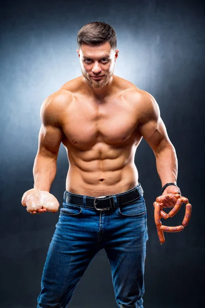 Muscular young sportsman holding chicken breasts and sausage. Dieting and sport nutrition, naked torso, athletic man. Closeup