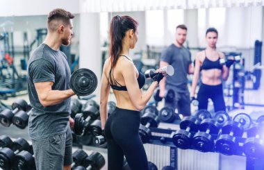 Spor, vücut geliştirme, yaşam tarzı ve insanların konsepti. Spor salonunda halter esneten genç erkek ve kadın. Antrenör ve fitness kızı spor salonunda antrenman yapıyor..