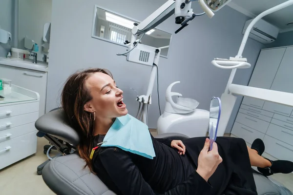 Visão traseira acima da jovem mulher deitada na cadeira dentária com boca aberta e olhando em linha reta. Conceito de procedimento odontológico e estomatologia. — Fotografia de Stock