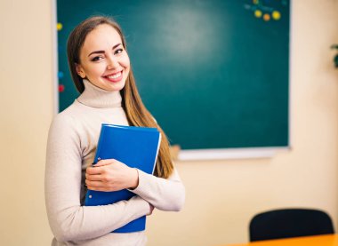 Sınıfta elinde dosyayla temiz bir tahtanın yanında duran öğrenci kız. Okul kavramı.