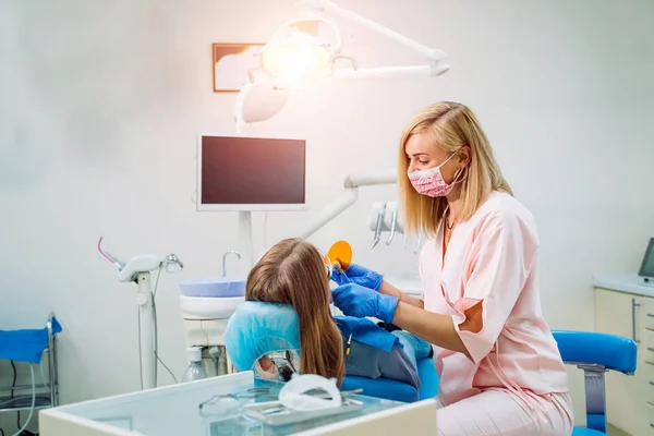 Dentista usando luvas e máscara examinar os dentes de um paciente com uma sonda dentária e um espelho em uma caixa clínica com equipamentos no fundo — Fotografia de Stock