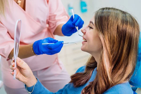 站在快乐的女病人身边，看着镜子，在牙科诊所里享受着美丽的微笑。牙科和口腔医学的概念. — 图库照片