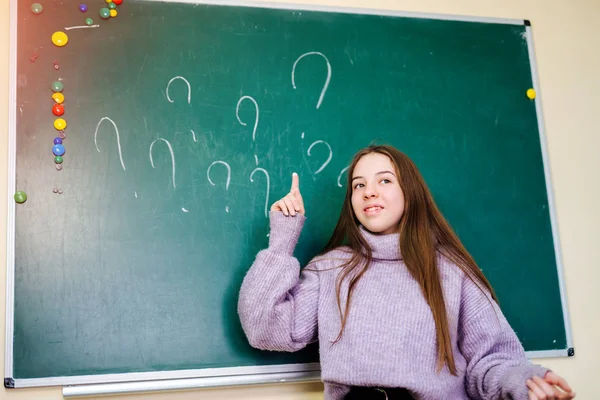 Een vraagteken op schoolbord, een leuk meisje wijst erop. Schoolonderwijsconcept. — Stockfoto