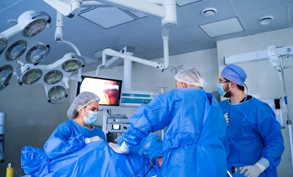 Eine Gruppe von Ärzten führt eine Operation an einem Patienten durch. Chirurgen in Uniform und Masken im Operationssaal — Stockfoto