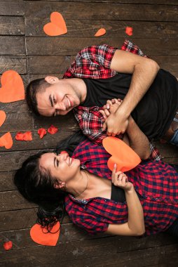 Üstten Görünüm mutlu genç çiftin birbirine bakarak ve ahşap yerde yatarken gülümseyerek. Kız bir kırmızı kağıt kalp tutuyor