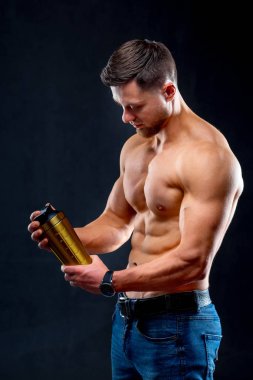 Güçlü kasları olan yakışıklı genç bir adam protein içeceği tutuyor. Güçlü kaslar. Koyu arkaplanda fitness kaslı vücut
