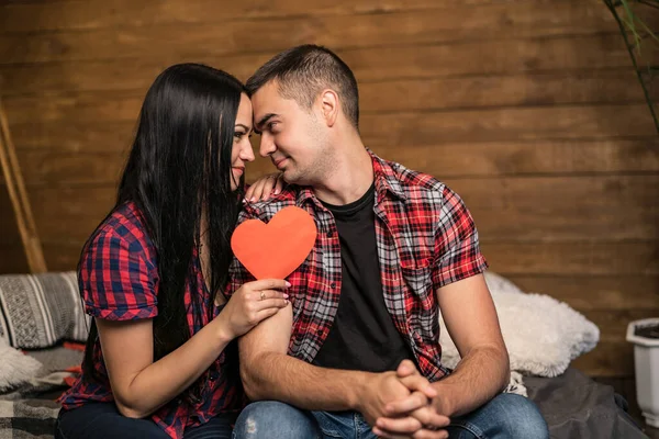 Hermosa pareja romántica en el fondo de la pared de madera. Una joven y atractiva y un hombre guapo abrazan con el corazón rojo en las manos. Concepto del Día de San Valentín — Foto de Stock