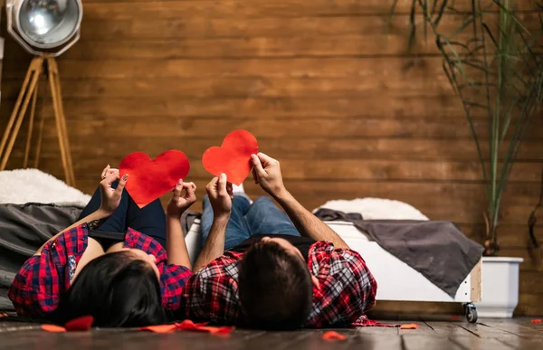 Celebrar el amor. Hermosa pareja de jovencitos enamorados unidos entre sí y sosteniendo papel de forma cardíaca mientras se pone en el suelo.. — Foto de Stock