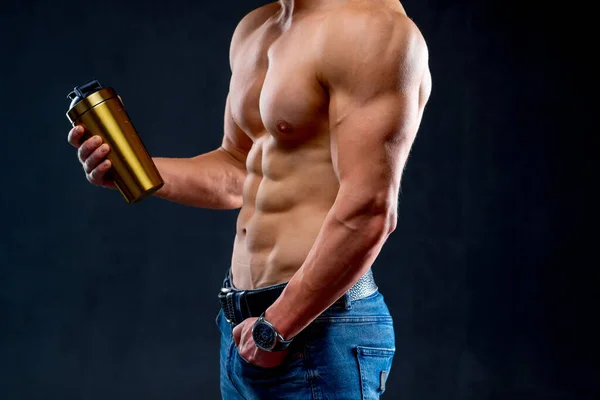 Спортсмен наполовину голий спортсмен у джинсах тримає пляшку води. Обрізана фотостудія в приміщенні. Крупним планом . — стокове фото